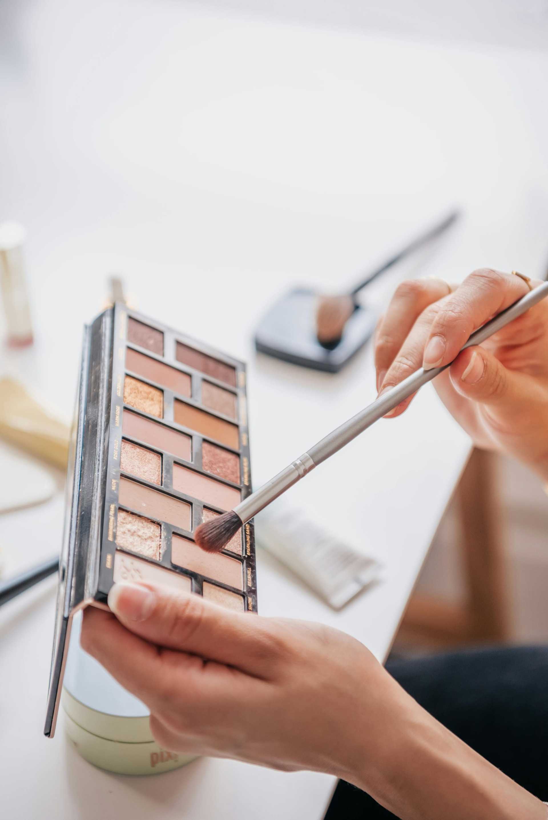 Applying eyeshadow with a brush from a colorful makeup palette.