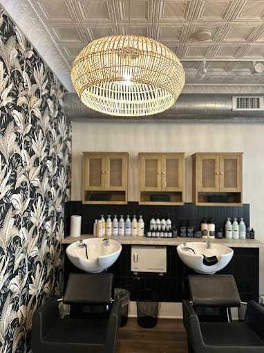 Modern salon interior with floral wallpaper, wicker chandelier, and shampoo stations.